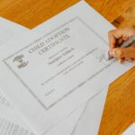 Close-up view of a hand signing an official child adoption certificate document.