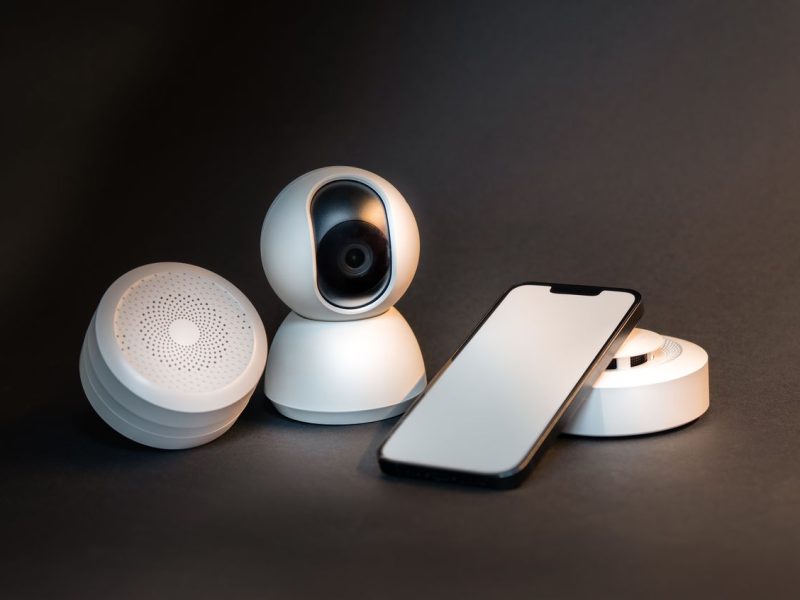 A sleek smartphone with modern smart home devices on a minimalist gray background.