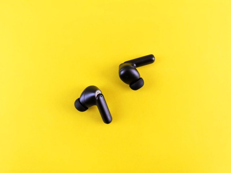 Minimalist black wireless earbuds on a bright yellow backdrop for tech and lifestyle themes.